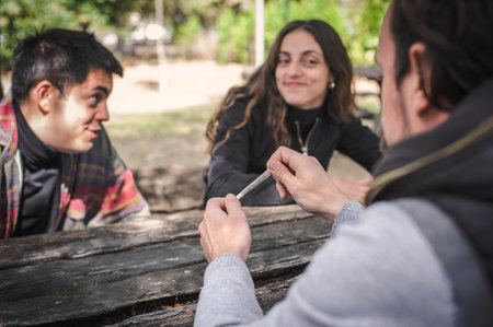 One friend shows the others excited happy friends a wrapped marijuana ganja or hashish joint ready to use. Closeup detail view. Young people smoke cannabis thc grass. Real life scene conceptの写真素材