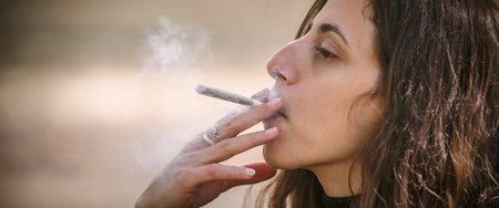 Closeup detail view of young woman smoke cannabis marijuana ganja or hashish joint cigarette. Casual...