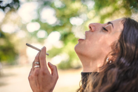 Closeup detail view of young woman smoke cannabis marijuana ganja or hashish joint cigarette. Casual...