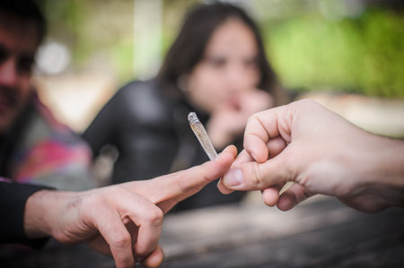 Closeup detail macro view of marijuana joint circling around from hand to hand. Young friends smoking cannabis marijuana ganja or hashish cigarette. Real life scene conceptの写真素材