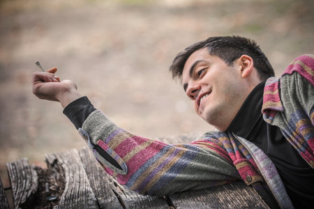 Close-up detail view of relaxed and smiling happy young man smoke cannabis marijuana ganja or hashish joint cigarette. Casual male smoking thc green grass. Real life scene conceptの写真素材