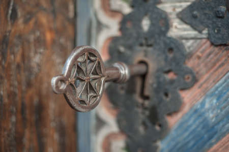 Closeup detail view of old massive metal key in a large huge church wooden ancient door. Secret mystery entrance. Traditional gothic grunge vintage style. Medieval security and safetyの写真素材