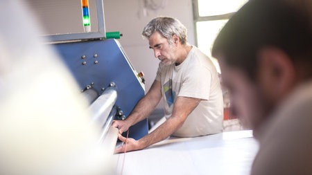 Two technician workers operator works on large premium fabric industrial textile sublimation roller...