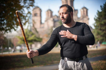 Escrima and kapap instructor demonstrates sticks fighting techniques in public park. Filipino Martial Arts. Eskrima. Kali.の写真素材
