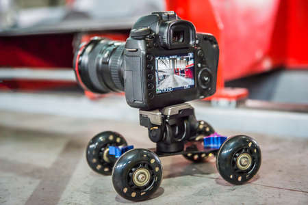 DSLR camera with monitor on mini table desktop rail wheel system making video of machine at factory. Car dolly skater truck. Professional digital equipmentの写真素材