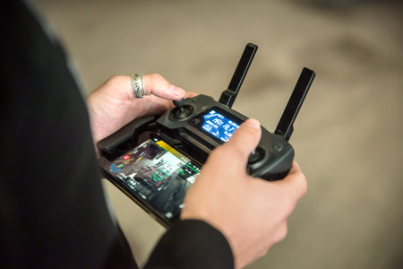 Man hands holding transmitter with attached mobile phone device and controlling FPV drone. Drone...