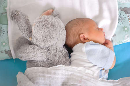 Cute little peaceful baby calm sleeps soundly in his crib with his baby toys in a bright room. Close-up portrait of beautiful child sleeping and restingの写真素材