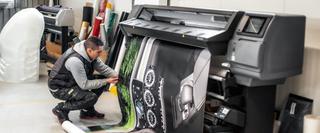 Technician worker operator works on large premium industrial printer and plotter machine in digital...