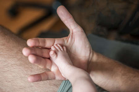 Close-up detail of parent holding cute and soft baby small leg in his hands. Macro abstract view of sweet baby foot fingers. Soft child skin feet. Love and family emotionの写真素材