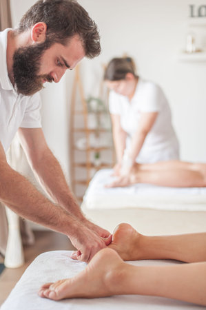 A man and a woman, professional masseurs are giving a foot massage in a spa center