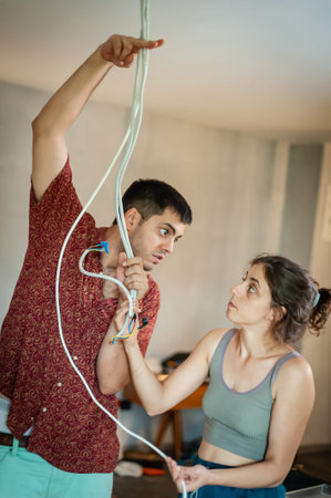 Living together concept, young man and woman have a problem with electric cables from the ceiling