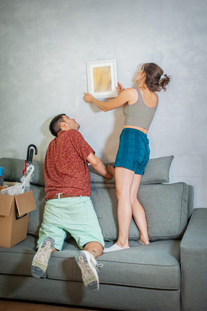 Cheerfully young couple decorates their new apartment with painting on the wall
