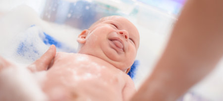 Baby bath time. Close-up detail view of mother bathing cute little peaceful baby in tub with water and bubbles latherの写真素材