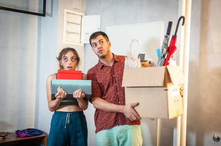 A young couple moves into their new apartment. They are surrounded by boxes, packages and other...