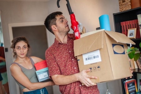 A young couple moves into their new apartment. They are surrounded by boxes, packages, colorful wardrobe and other things.の写真素材