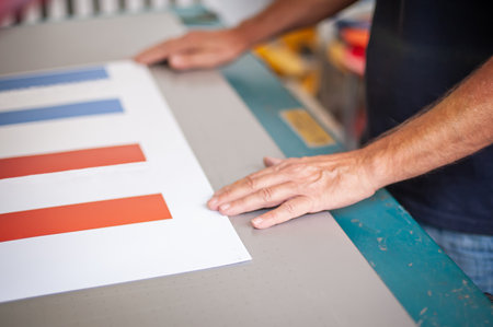 In the printing house, an experienced technician works on a screen printing machine. Production work. Check the print quality.の写真素材