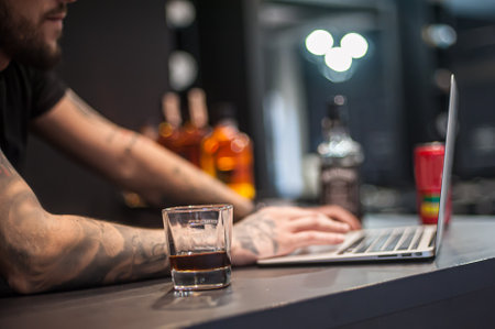 Young man drink whiskey and work on laptop computer. Close-up detail viewの写真素材
