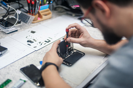 Workplace top view, close-up. Repairman disassembles smartphone with screwdriver in an electronics repair shop.の写真素材