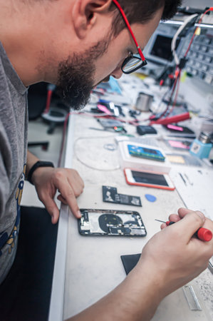 Workplace top view, close-up. Repairman disassembles smartphone with screwdriver in an electronics repair shop.の写真素材