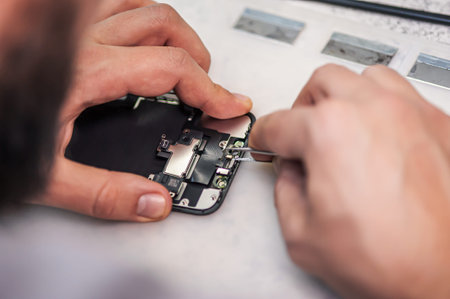 Workplace top view, close-up. In an electronics repair shop, a repairman repairs a smartphone, uses...