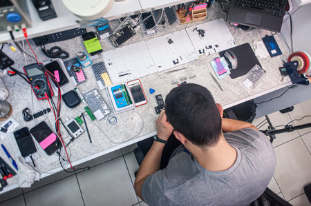 Electronics repair shop, a repairman is surrounded by tools and equipment. A technician repairs, cleans, controls a smartphone. Workplace top view, close-up.の写真素材