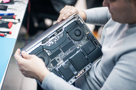 Technical support and fixing gadgets problems. Servicing, repairing, cleaning, maintaining computers. Repair shop. Hardware maintenance. Male technicians fixing disassembled laptop parts.の写真素材