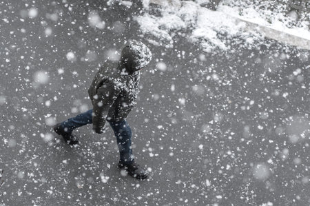People walks on the urban city street on a snowy winter day with small white snow snowflakes in...