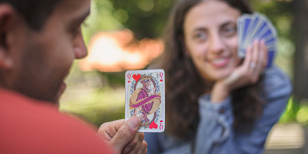 Card playing in a spring garden: Couple are sitting on a table, relaxing and playing cards together. Blurry background.の写真素材