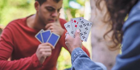 Card playing in a spring garden: Couple are sitting on a table, relaxing and playing cards together. Blurry background.の写真素材
