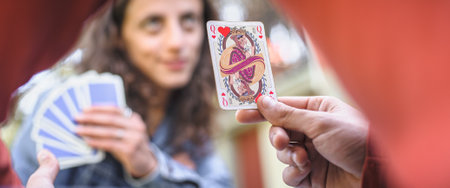 Card playing in a spring garden: Couple are sitting on a table, relaxing and playing cards together. Blurry background.の写真素材