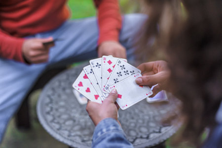 Card playing in a spring garden: Couple are sitting on a table, relaxing and playing cards together. Blurry background.の写真素材