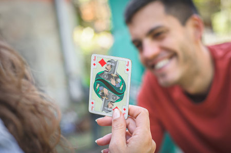 Card playing in a spring garden: Couple are sitting on a table, relaxing and playing cards together. Blurry background.の写真素材
