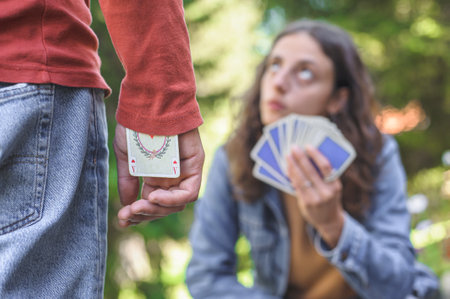 A young happy couple playing cards in a spring garden: the young man hides an ace in his sleeve.の写真素材