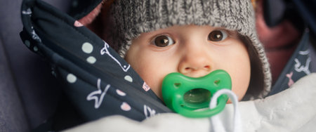 Portrait view of cute little peaceful baby with pacifier in winter jacket and hat. Joy and happiness...