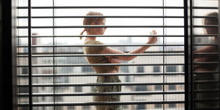 Influencer teenage girl in the city behind open horizontal aluminum metal black blinds, using a smartphone. Close-up, window background. Back view, bright, texture.の写真素材