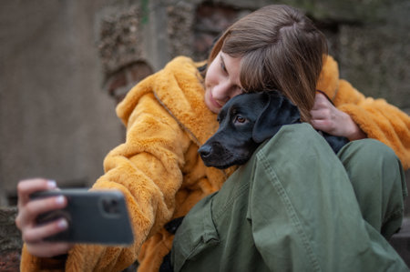 Influencer, teenage girl with a black dog taking a selfie with her smartphone, outdoors in the city streetsの写真素材