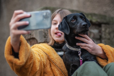 Influencer, teenage girl with a black dog taking a selfie with her smartphone, outdoors in the city streetsの写真素材