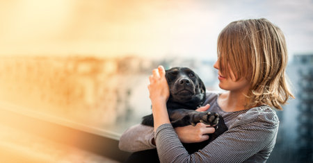 A pretty teenage girl hugs her black dog on the terrace of a solitaire in the cityの写真素材