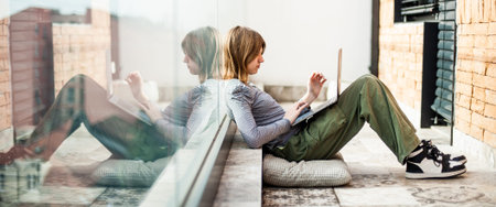 Beautiful teenage social media influencer sitting on patio floor using laptop for studying and entertainmentの写真素材