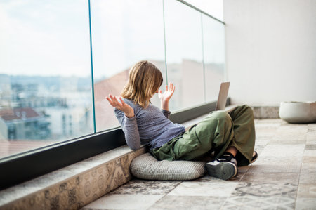 Beautiful teenage social media influencer sitting on patio floor using laptop for studying and entertainmentの写真素材