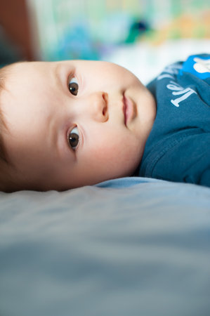 Portrait of cute baby boy lying on bed and looking at camera. Place for text. Love and family emotionの写真素材