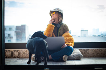 Hipster teenage girl sitting with laptop on terrace with view on city. Young happy woman in hat using laptop, shopping or working online from home outdoors. Freelance and freelancer.の写真素材
