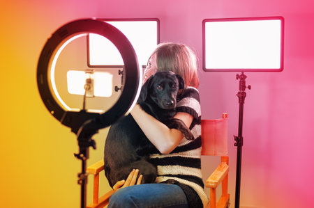 Romantic photo of a dog in the warm embrace of its owner. Friends forever. Blank empty space, colorful room and lighting background. Radio host, charming influencer girl, records a live show with camera stuff and equipment.の写真素材