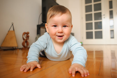 Portrait of cute happy smiling baby boy crawls on the home floor and looking at camera. Joy and happiness concept. Love and family emotionの写真素材