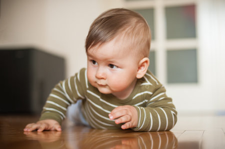 Cute baby boy crawls on the home floor, explore the world and learn to move. Front view. Love and family emotionの写真素材