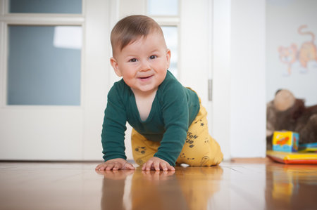 Portrait of cute happy smiling baby boy crawls on the home floor and looking at camera. Joy and happiness concept. Front view. Love and family emotionの写真素材