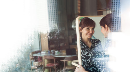 Contemporary modern woman, brunette, in a dress, standing in front of the mirror in her comfortable...