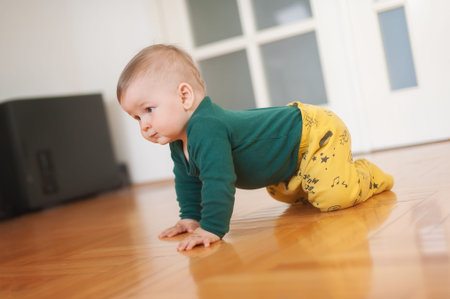 Cute baby boy crawls on the home floor, explore the world and learn to move. Side view. Love and family emotionの写真素材