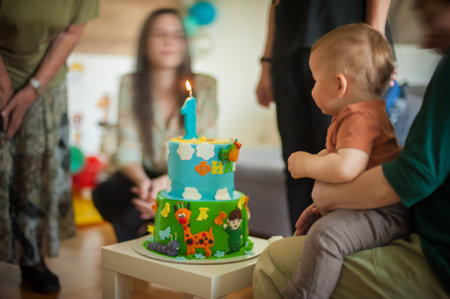 Cute baby boy celebrates his first birthday with his family at home. Cake and candle in the shape of number oneの写真素材