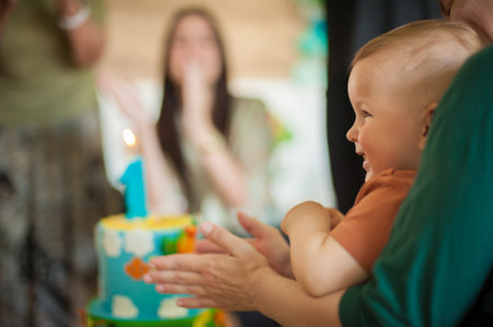 Cute baby boy celebrates his first birthday with his family at home. Cake and candle in the shape of number oneの写真素材